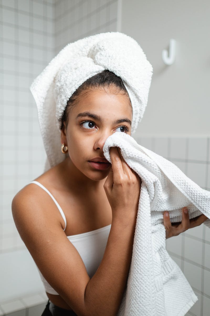 Woman in White Tank Top Wiping Her Face With Towel